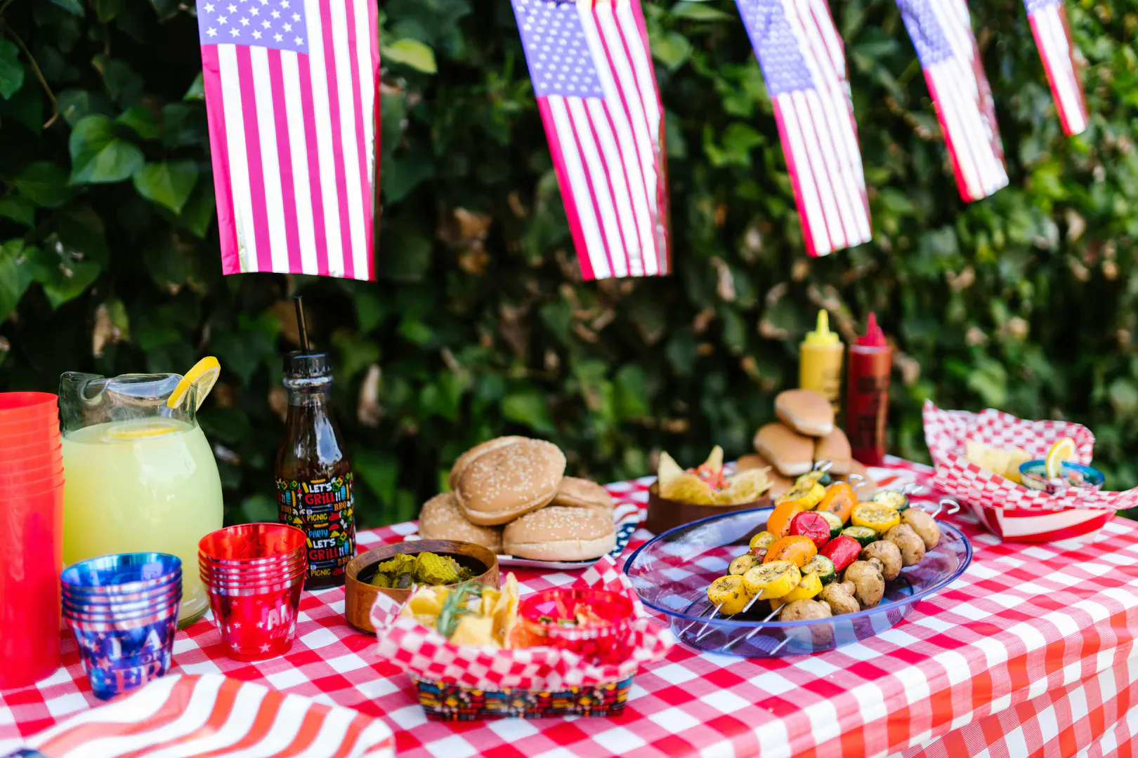 A Fourth of July backyard picnic table set with American flags for a summer cookout