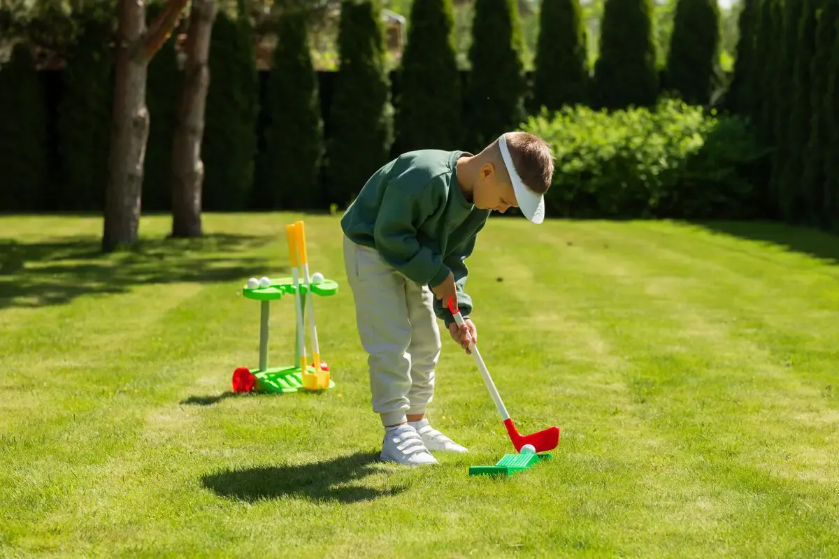 Young boy chipping a ball with a toy golf club set on a backyard lawn