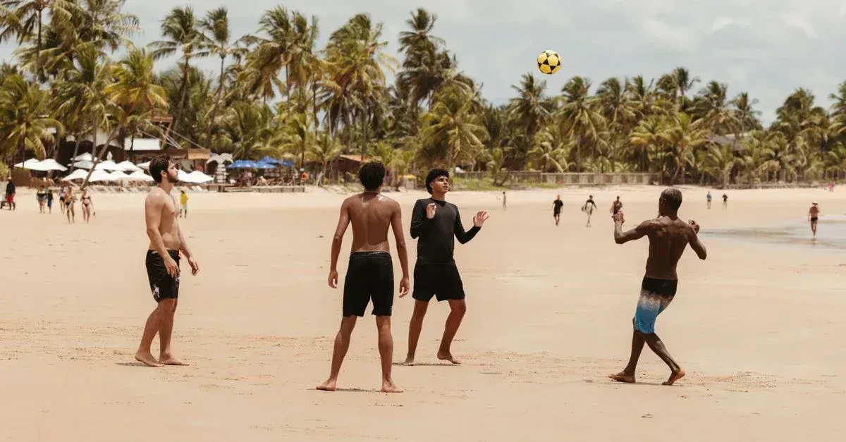 Friends playing Spikeball and paddle ball on a sunny sandy beach with the ocean behind them