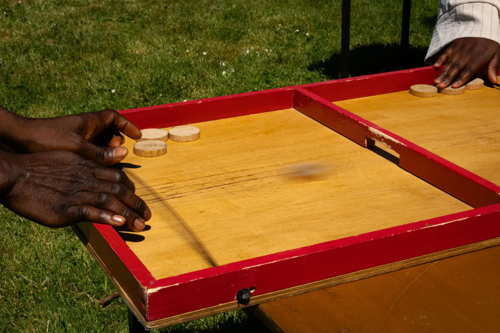 A wooden three-hole washer toss board on a backyard lawn with metal washers nearby, the kind of set that makes the best washer toss game