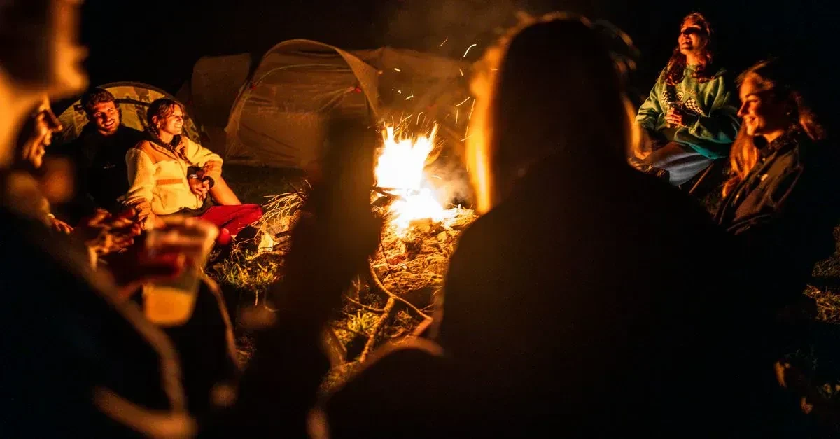 Adults playing the best camping games for adults around a campsite at dusk with tents and a campfire glow