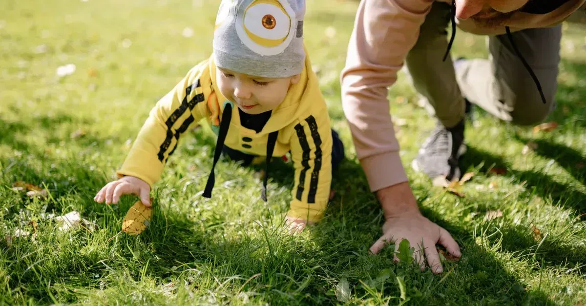 Happy toddlers playing with soft colorful outdoor toys on a grassy lawn with a parent nearby, the best outdoor games for toddlers in action