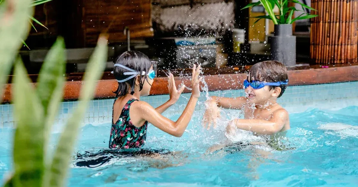 Kids and adults playing volleyball and dive games in a backyard swimming pool on a bright sunny day
